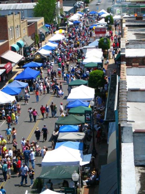 A bustling street fair with numerous tents and crowds of people enjoying the festivities under a clear blue sky.