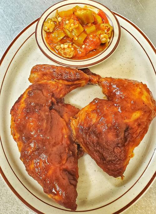 Two pieces of glazed chicken on a plate, accompanied by a bowl of okra and tomato stew.
