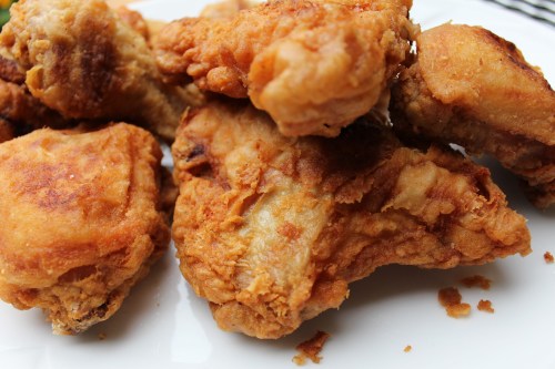 A close-up of crispy, golden-brown fried chicken pieces on a white plate.