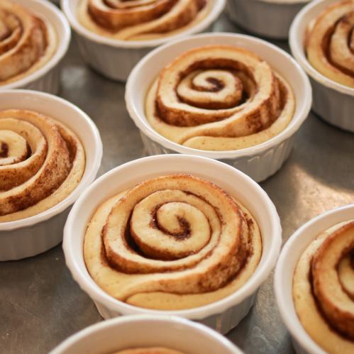 Freshly baked cinnamon rolls in white ramekins, showcasing their swirled, golden-brown tops.