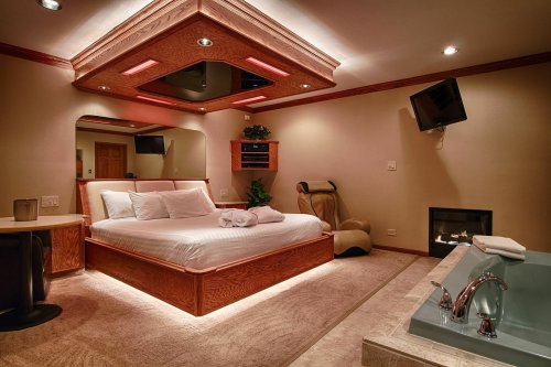 Cozy bedroom with a large bed, soft lighting, a fireplace, and a relaxing seating area.