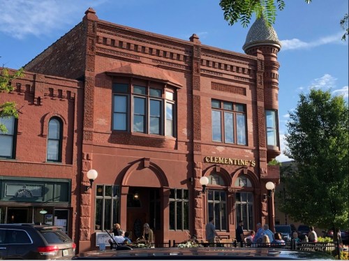 Historic red brick building with large windows, featuring a turret, and outdoor seating at Clementine's restaurant.