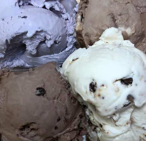 A close-up of various ice cream flavors, including chocolate, vanilla, and grayish tones, in a container.