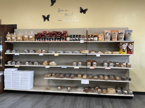 A display shelf filled with various baked goods, snacks, and packaged treats in a cozy shop setting.