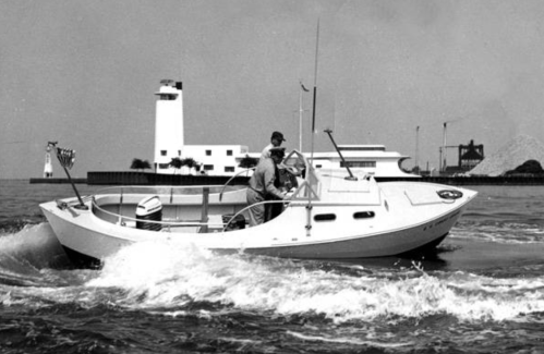 A vintage boat with two people navigating through water, with a lighthouse and buildings in the background.