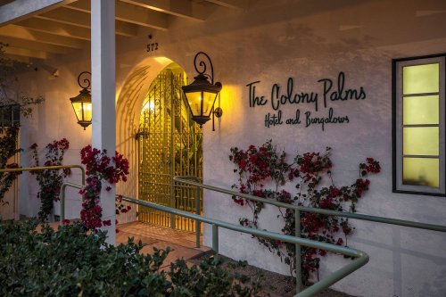 Entrance of The Colony Palms Hotel and Bungalows, featuring decorative lanterns and blooming vines.
