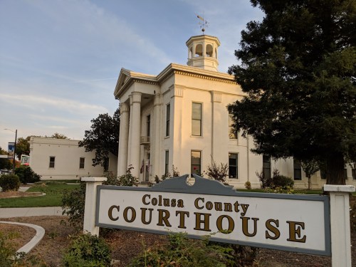Colusa County Courthouse with a sign in front, featuring classical architecture and surrounding greenery.