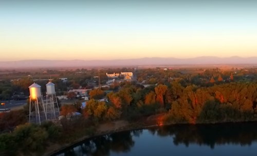 Aerial view of a serene landscape at sunset, featuring water towers, trees, and a calm pond.