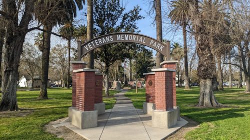 Entrance to Veterans Memorial Park, featuring a brick archway and a pathway lined with trees and greenery.