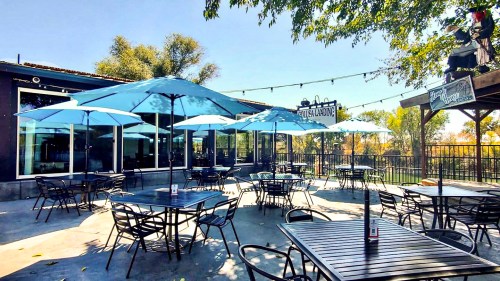 Outdoor dining area with blue umbrellas, tables, and a view of trees under a clear sky.