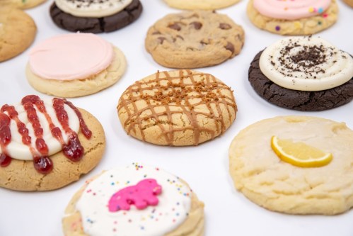 A variety of colorful cookies with different toppings and flavors arranged on a white surface.