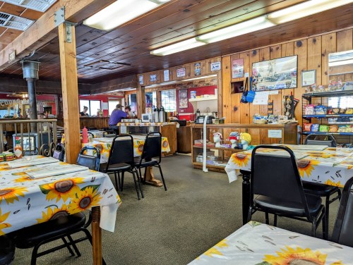 Cozy diner interior with sunflower tablecloths, wooden walls, and a counter displaying snacks and drinks.