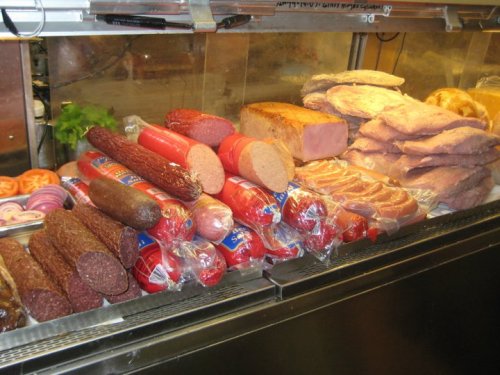 A display of various packaged meats, including sausages, ham, and loaves, arranged neatly in a refrigerated case.