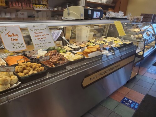 A display case filled with various prepared foods, including chili, pastries, and side dishes, in a cozy eatery.