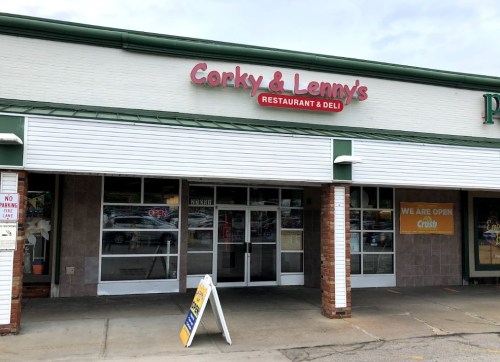 Exterior of Corky & Lenny's Restaurant & Deli, featuring a sign and an open door, with a parking lot visible.