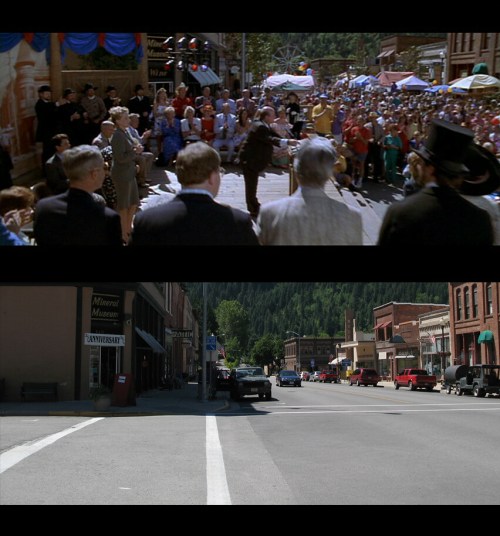A bustling town square filled with people, with a parade and historic buildings in the background.