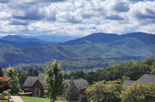 A scenic view of rolling green mountains under a partly cloudy sky, with houses in the foreground.