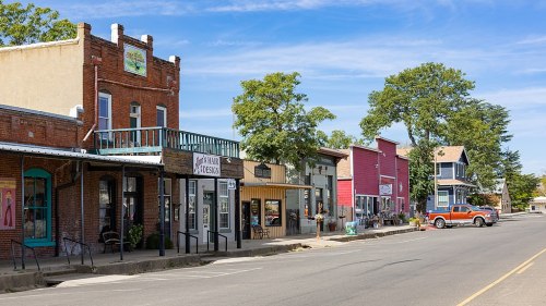 A charming small-town street lined with colorful storefronts and trees under a clear blue sky.