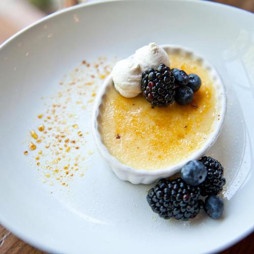 A creamy dessert topped with blackberries, blueberries, and whipped cream, served in a white dish with caramelized sugar.