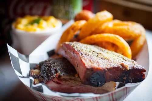 A plate featuring smoked meat slices, curly fries, and a side of macaroni and cheese in a checkered basket.