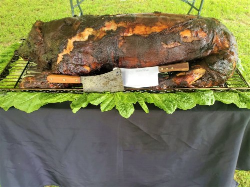 A whole roasted pig on a grill, surrounded by lettuce, with a large cleaver resting beside it.