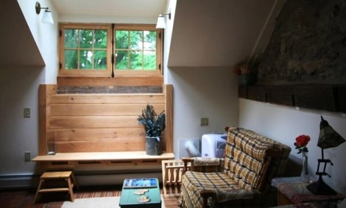 Cozy interior with a wooden bench, plaid chair, and large windows letting in natural light.