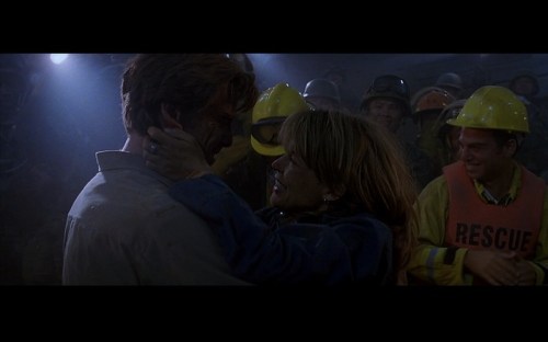 A joyful reunion between two people in a rescue scene, surrounded by smiling rescue workers in helmets and vests.