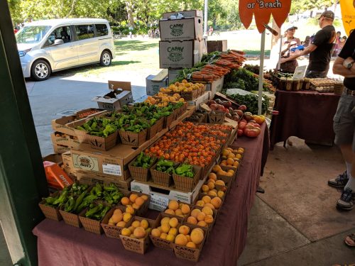 A vibrant farmers market display with various fruits and vegetables in baskets, including peppers, tomatoes, and peaches.