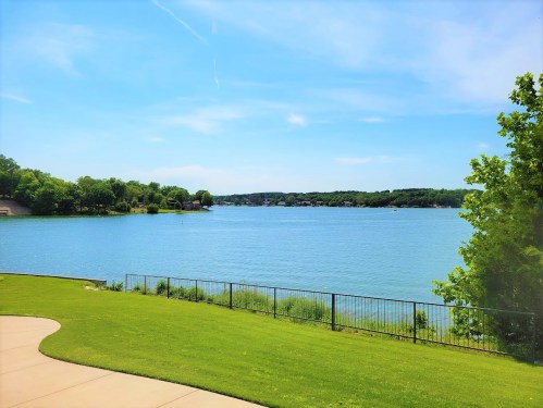 A serene lake view with clear blue water, green grass, and trees under a bright blue sky.