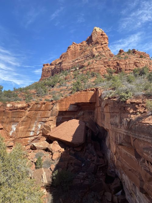 A rocky landscape featuring a prominent red rock formation under a blue sky with scattered clouds.