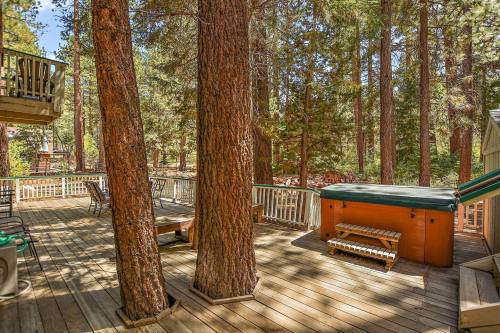 A wooden deck surrounded by tall trees, featuring a hot tub and seating areas in a serene outdoor setting.