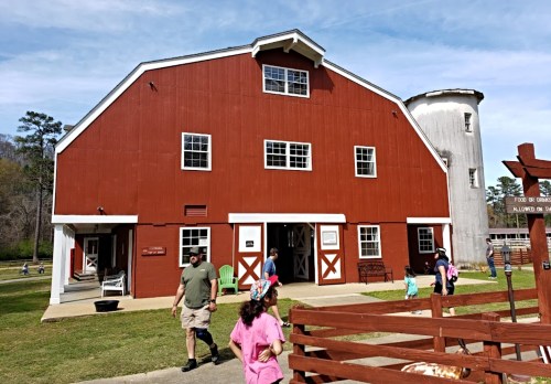 A red barn with white trim and a silo, surrounded by people enjoying a sunny day outdoors.