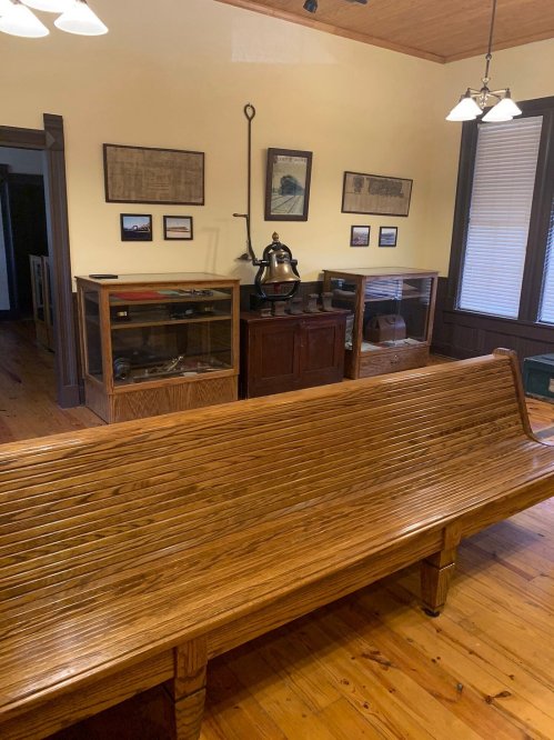 A wooden bench in a room with display cases, vintage items, and framed pictures on the walls.