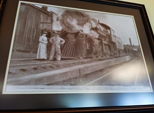 Black and white photo of two people standing beside a steam locomotive on train tracks.