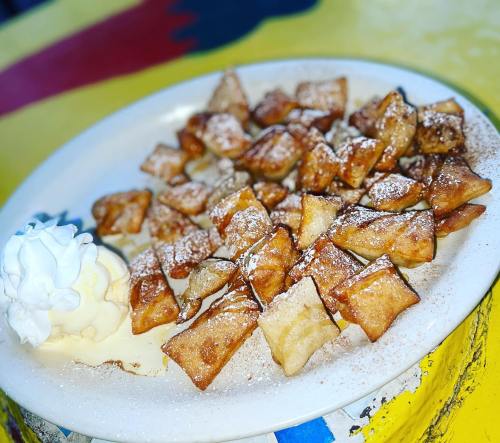 A plate of golden, crispy dessert pieces dusted with powdered sugar, served with a scoop of vanilla ice cream.