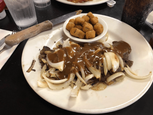 A plate of sliced beef topped with onions and gravy, accompanied by a bowl of fried snacks.