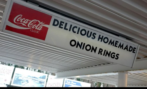 Sign advertising "Delicious Homemade Onion Rings" with a Coca-Cola logo above it.