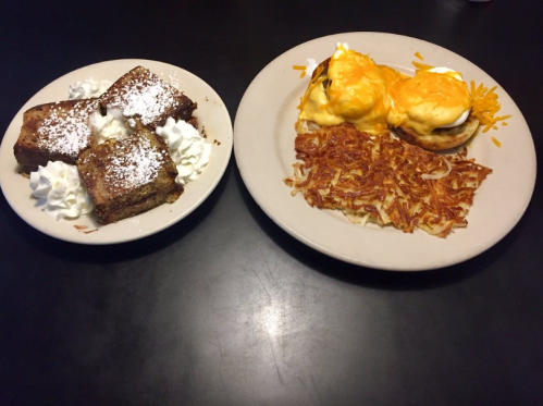 A plate with chocolate cake topped with whipped cream and a plate of eggs Benedict with hash browns and cheese.