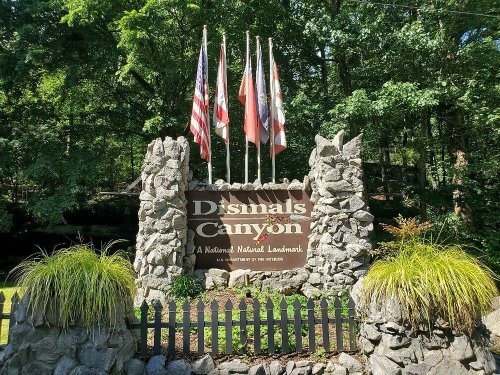 Sign for Dismals Canyon, featuring flags and surrounded by greenery, indicating it's a national natural landmark.