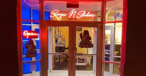 Brightly lit entrance of "Scoop N Shakes" with neon signs, featuring an "Open" sign and ice cream graphics on the door.
