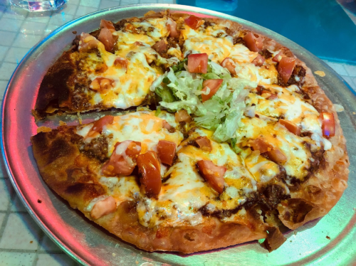 A pizza topped with cheese, tomatoes, lettuce, and ground meat, served on a metal tray.