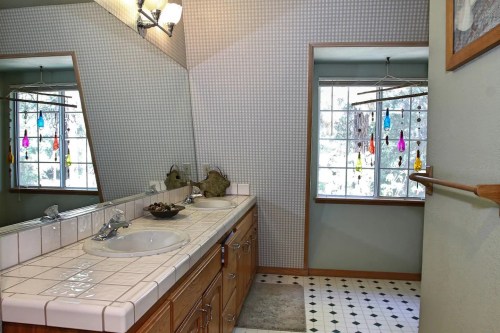 Bright bathroom featuring a tiled sink, large mirror, and colorful window decorations. Natural light from the window.