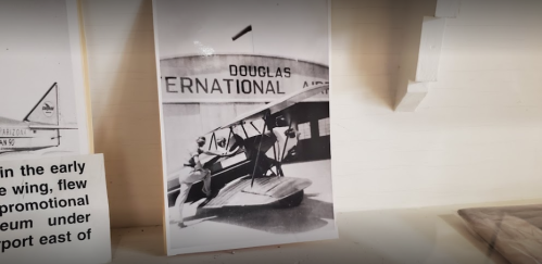 Black and white photo of a vintage airplane at Douglas International Airport, with a person standing beside it.