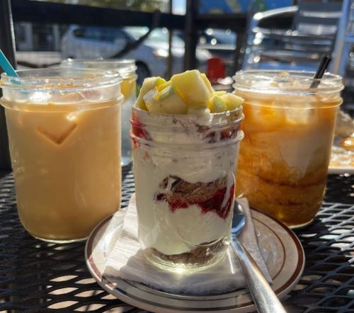 Three jars of desserts and drinks on a table: a layered parfait, a creamy drink, and a cold beverage with ice.