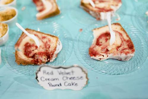 Slices of red velvet cream cheese pound cake on clear plates, with plastic forks and a label describing the dessert.