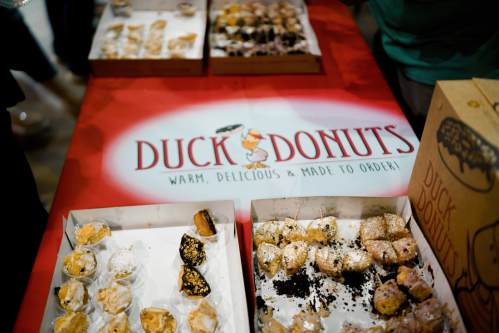 A table with boxes of assorted donuts from Duck Donuts, featuring a logo and the tagline "Warm, delicious & made to order."