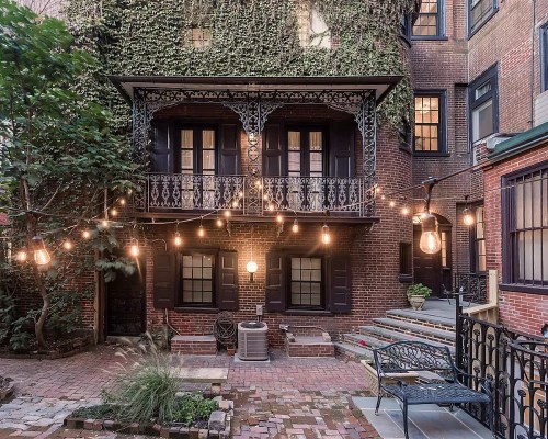 Charming courtyard with ivy-covered brick walls, vintage lights, and a wrought-iron bench. Cozy and inviting atmosphere.