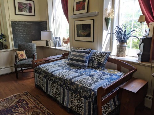 A cozy room featuring a daybed with blue patterned bedding, a chair, and large windows with natural light.