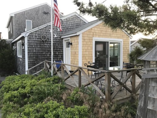 Cozy beach house with a wooden deck, American flag, and surrounding greenery.