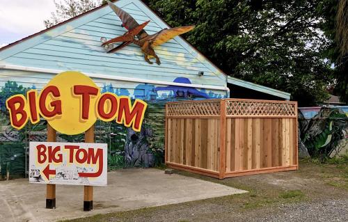 Colorful mural on a building with a large sign reading "BIG TOM" and a wooden enclosure nearby.